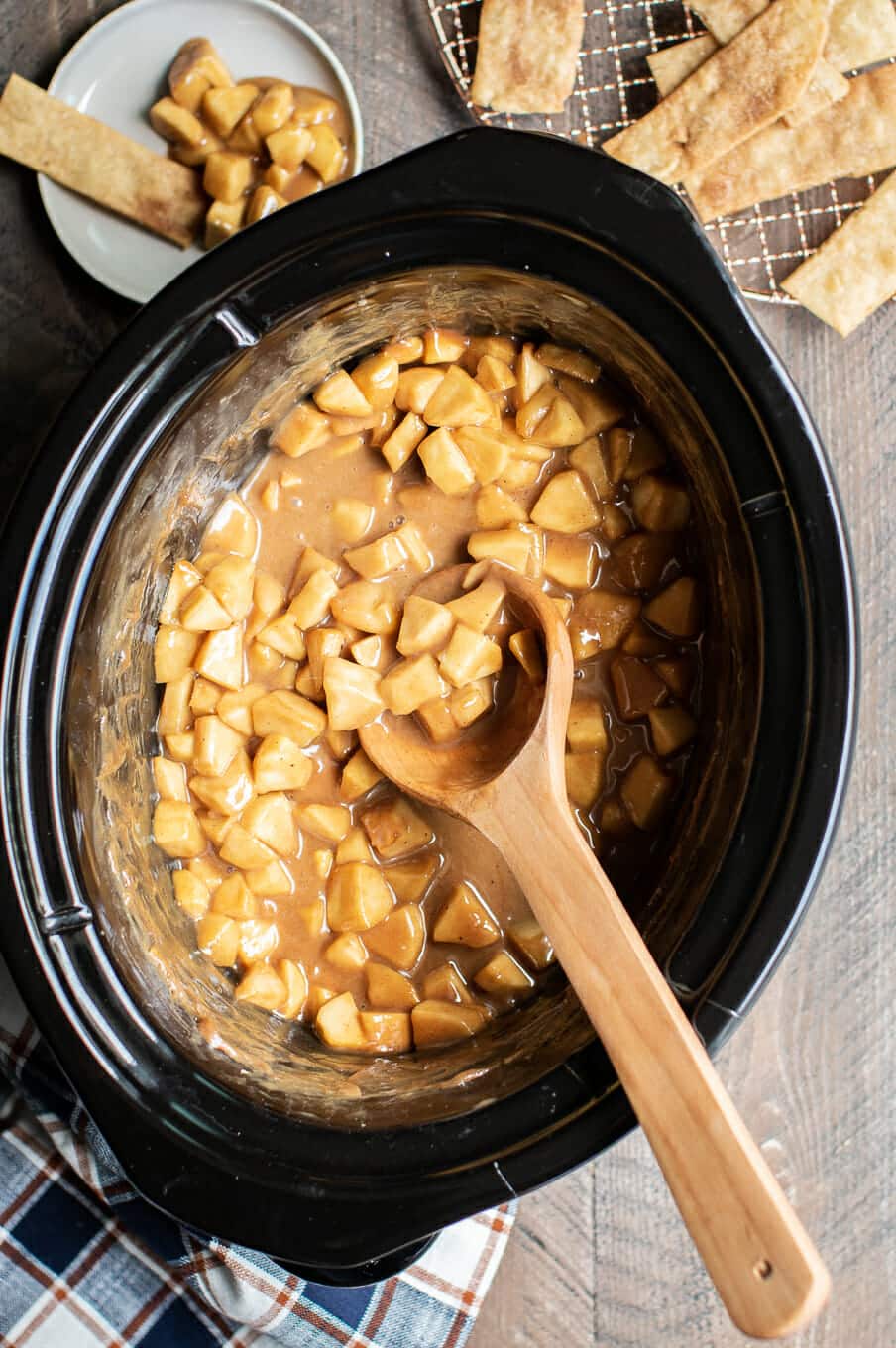Diced apples in slow cooker with caramel. Pieces of pie strips next to it.