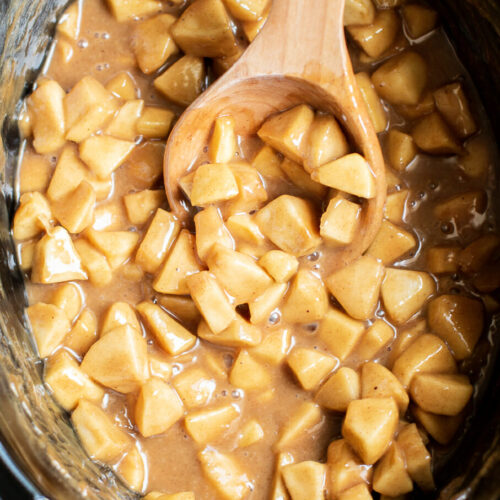 diced apples in caramel in slow cooker. Wooden spoon in it.