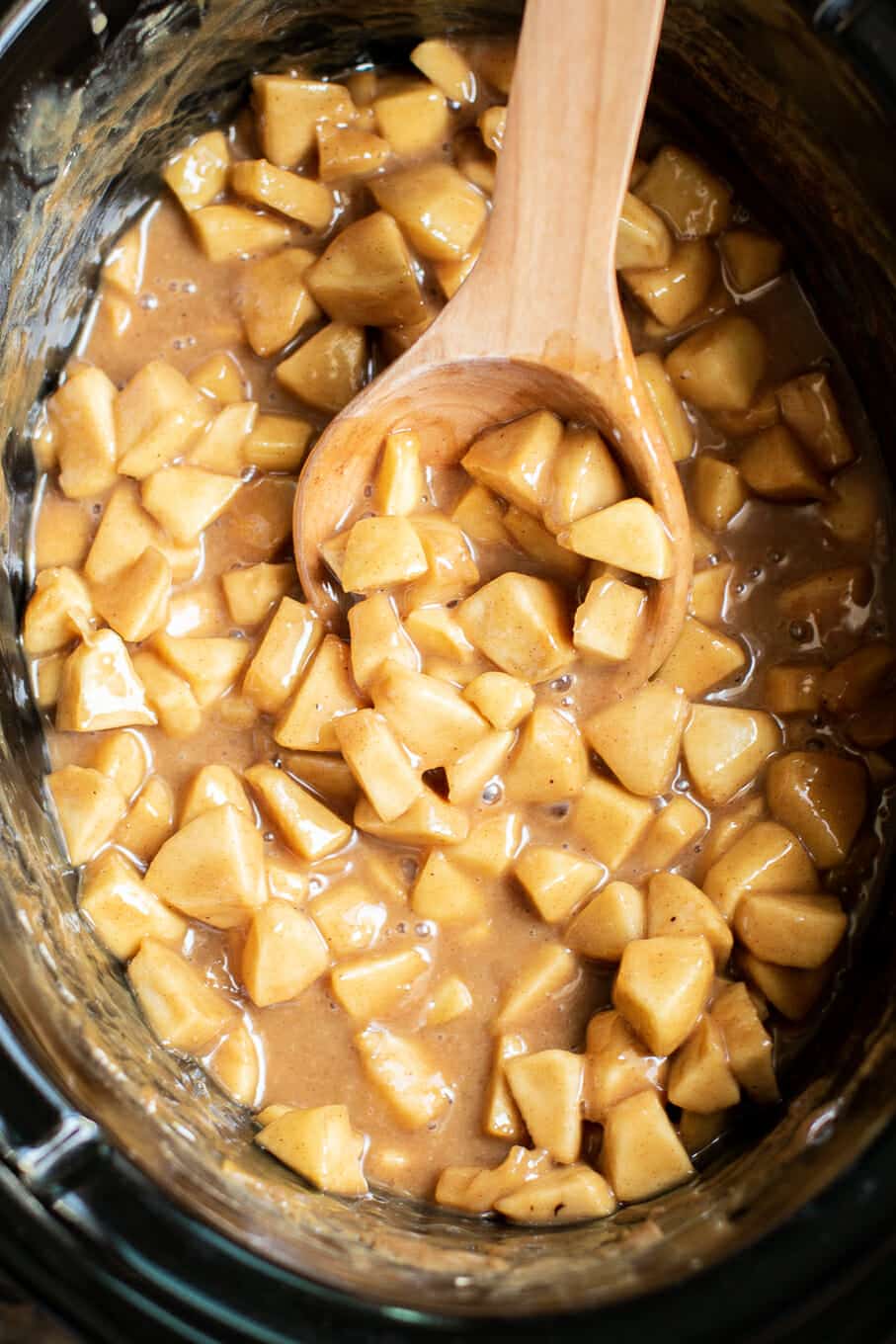 diced apples in caramel in slow cooker. Wooden spoon in it.