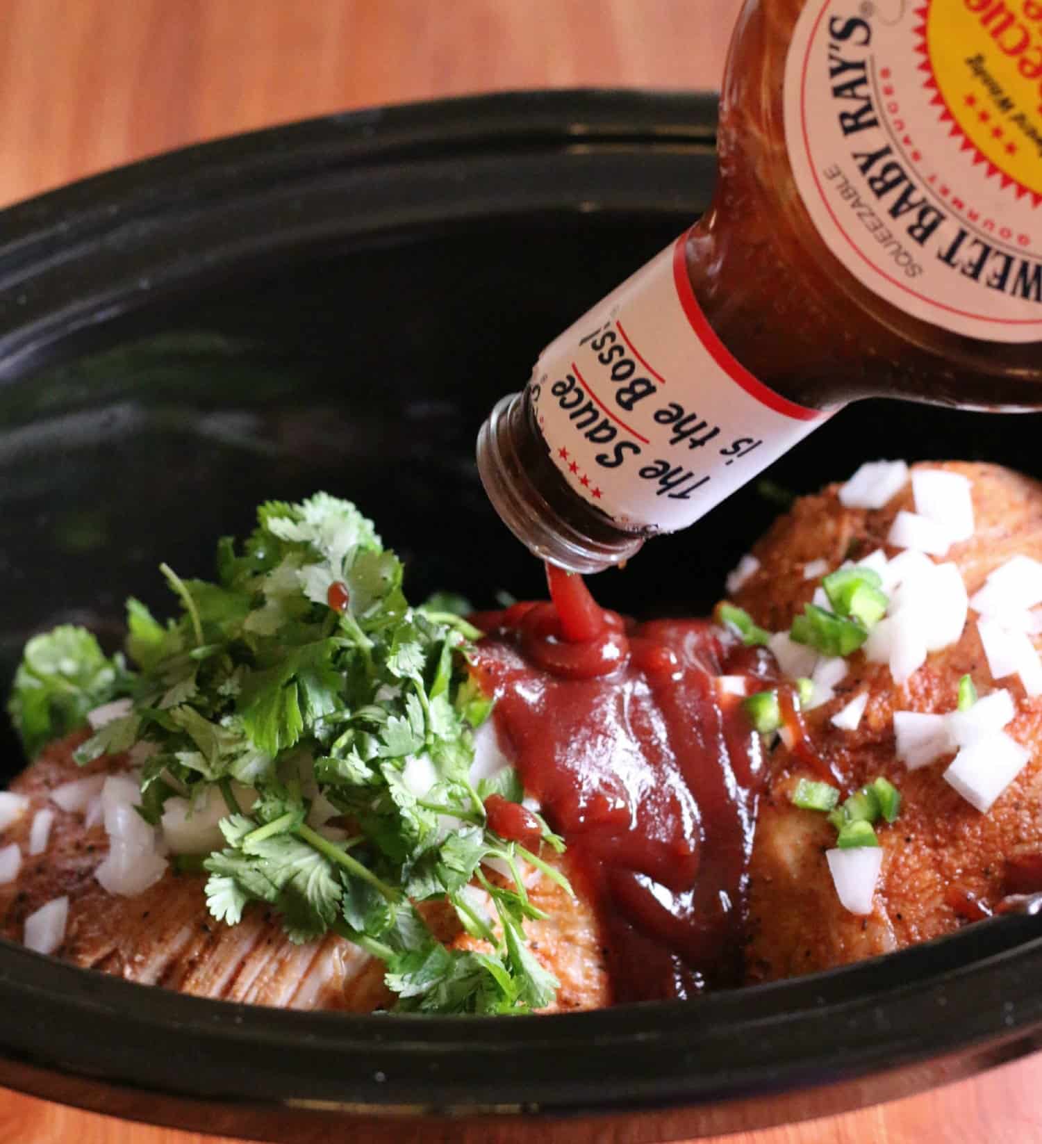 Pulled pork in crockpot with sweet baby ray's barbecue sauce being poured over