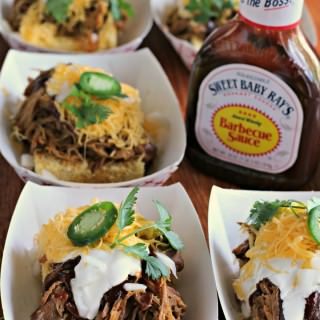 trays of cornbread with pulled pork on top. Bottle of sweet baby ray's barbecue sauce on side.