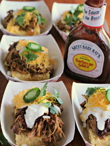 trays of cornbread with pulled pork on top. Bottle of sweet baby ray's barbecue sauce on side.