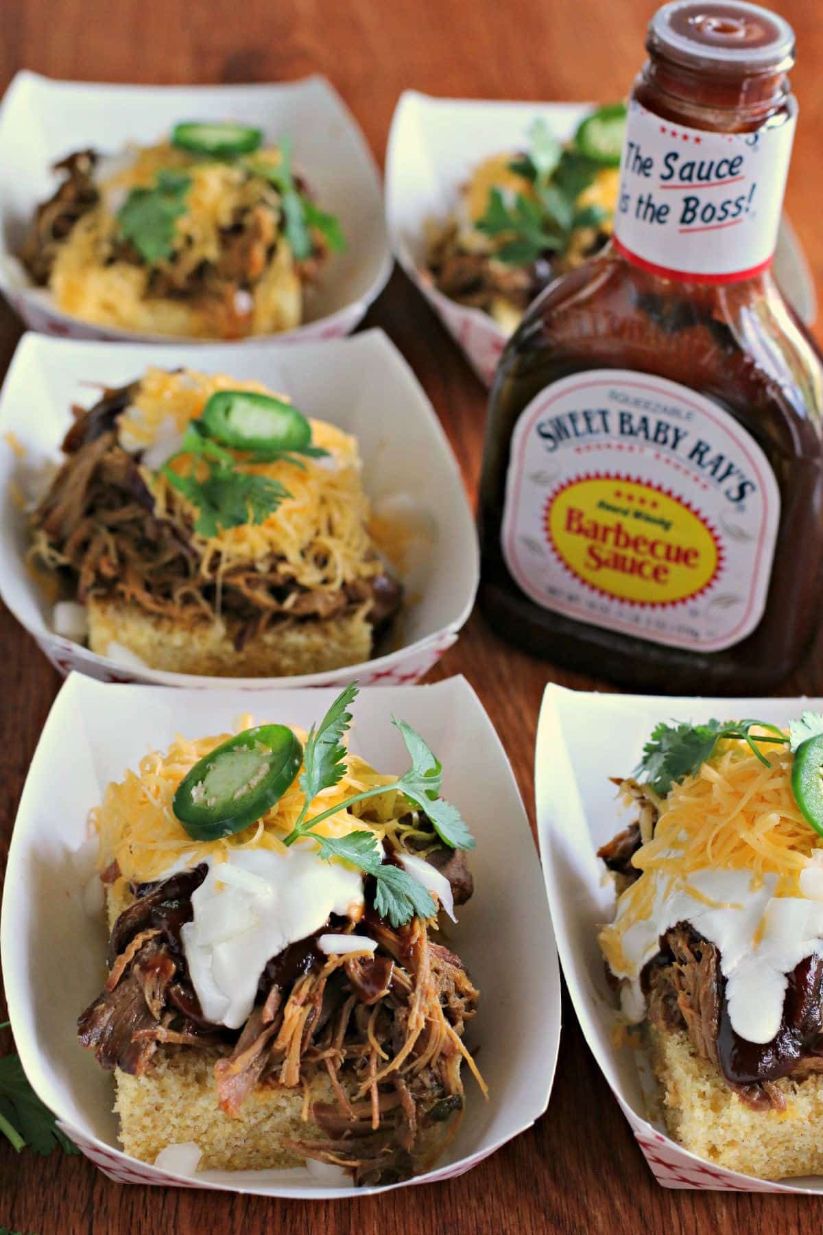 trays of cornbread with pork on top, barbecue sauce bottle on the side