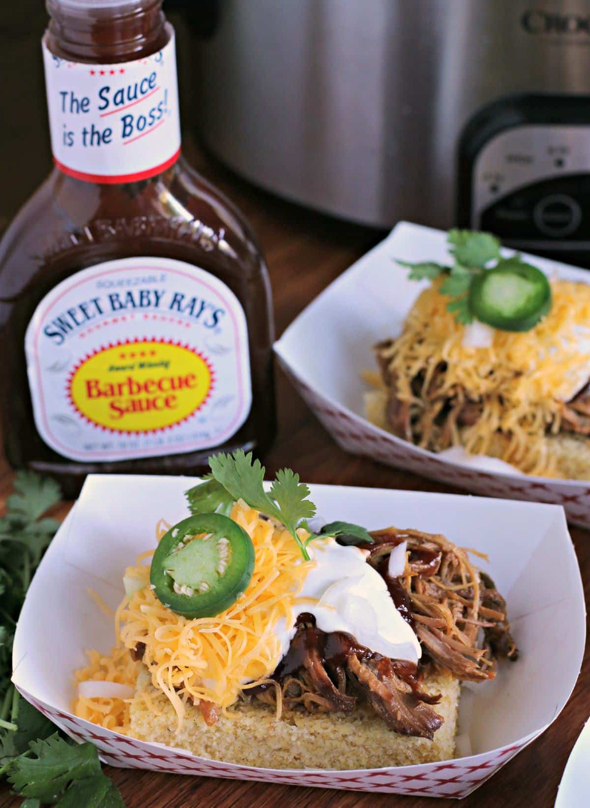 tray with cornbread and pork on top, barbecue sauce bottle on side.