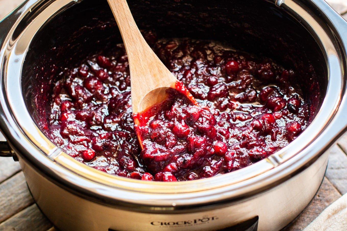 cooked cranberry sauce in the slow cooker with wooden spoon in it.