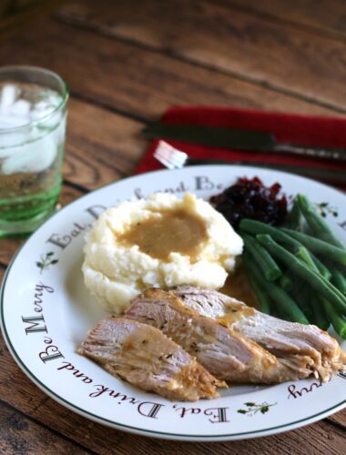 turkey breast slices with gravy with mashed potatoes, green beans and cranberry sauce on side.