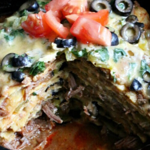 Beef and corn tortillas stacked together with cheese, tomato and olives on top.