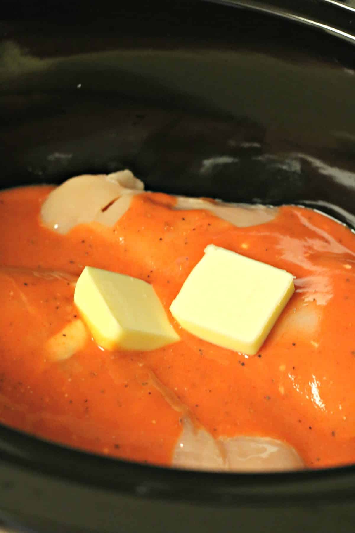 raw chicken in slow cooker with buffalo sauce and butter