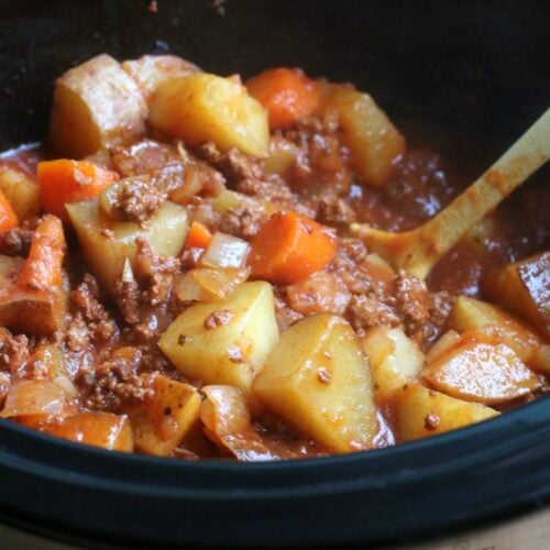 thick stew with potatoes and carrots in slow cooker with yellow spoon in it.