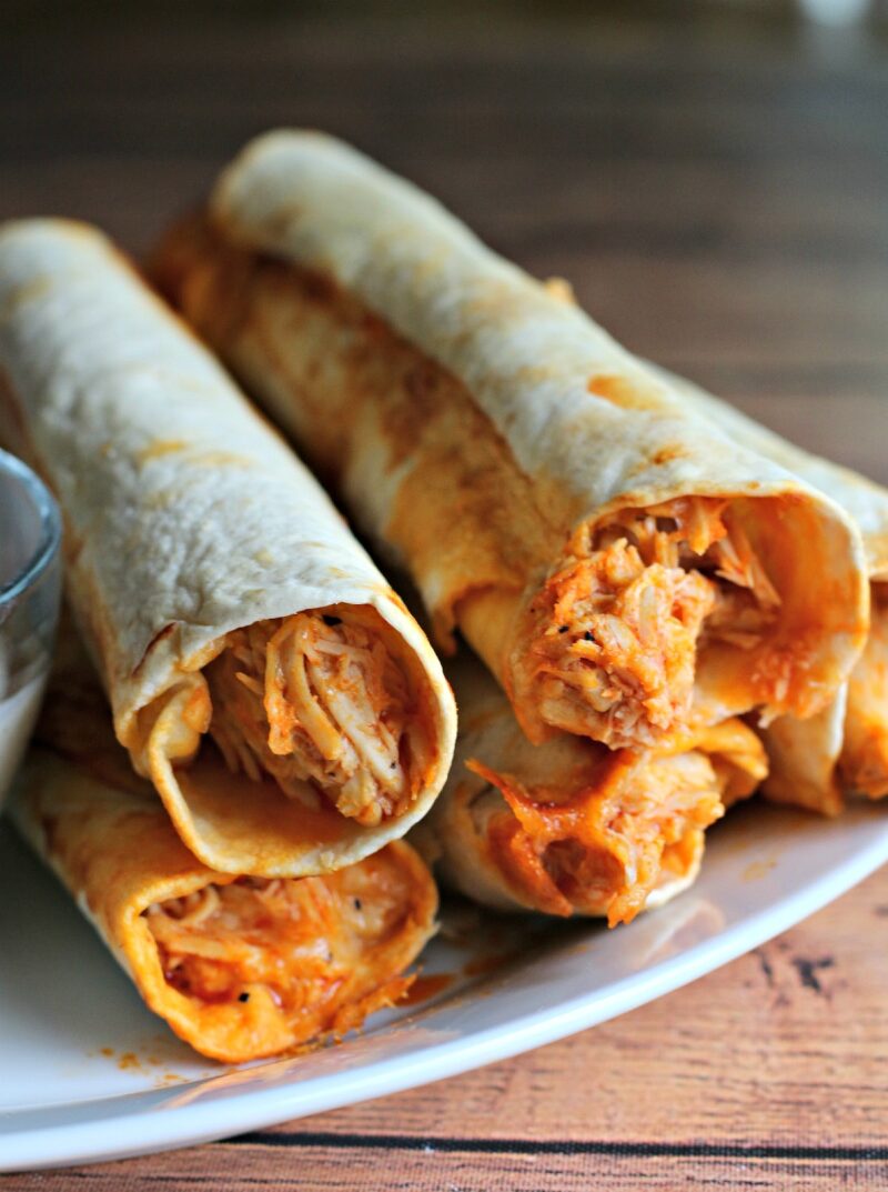 close up photo of stack of buffalo chicken flautas on a white plate