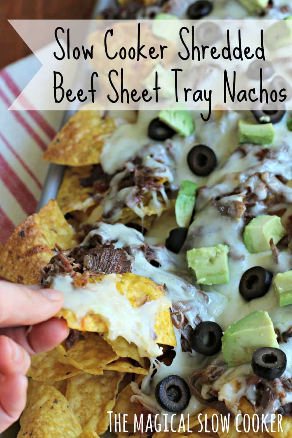 nachos on a sheet pan with cheese, olives and avocado on top.