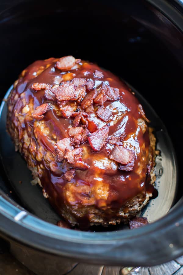 meatloaf in a slow cooker with barbecue sauce over it and bacon