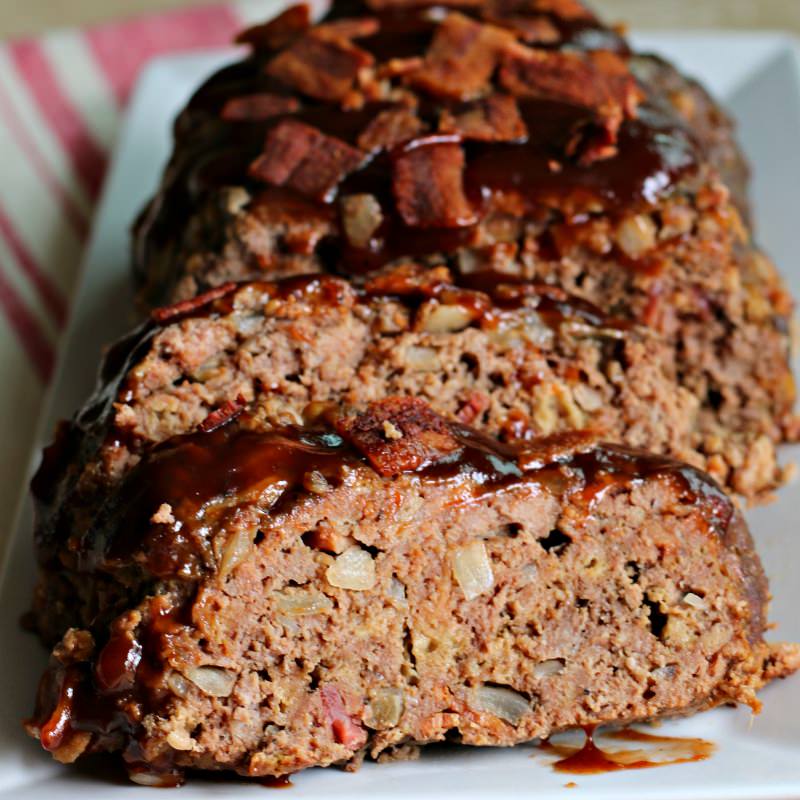 sliced meatloaf on a plate with bacon and barbecue sauce.