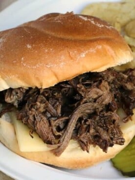 beef sandwich on plate with chips and pickles on side