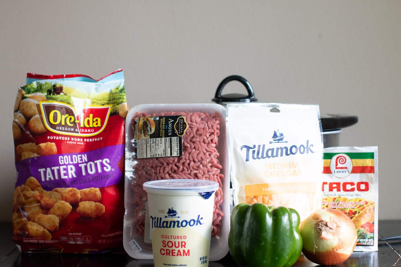 tater tots, ground beef, cheese, bell pepper, sour cream, and onion in front of slow cooker.