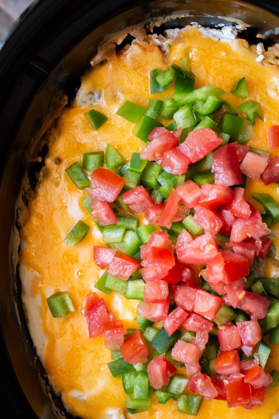 casserole in the slow cooker with bell pepper and tomato on top.