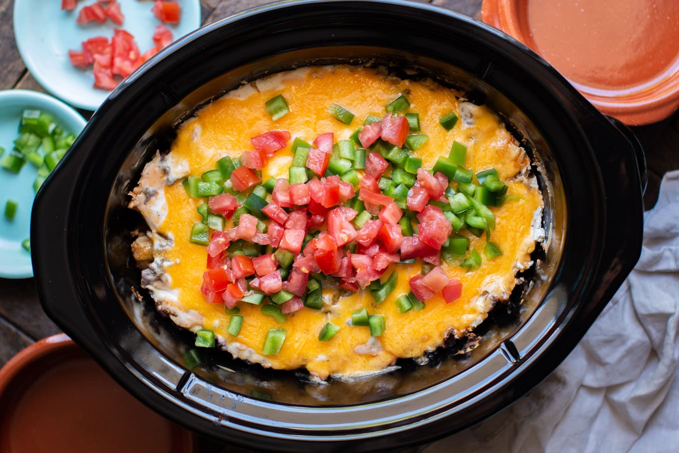 tater tot casserole in the slow cooker with cheese, bell pepper and tomatoes on top.