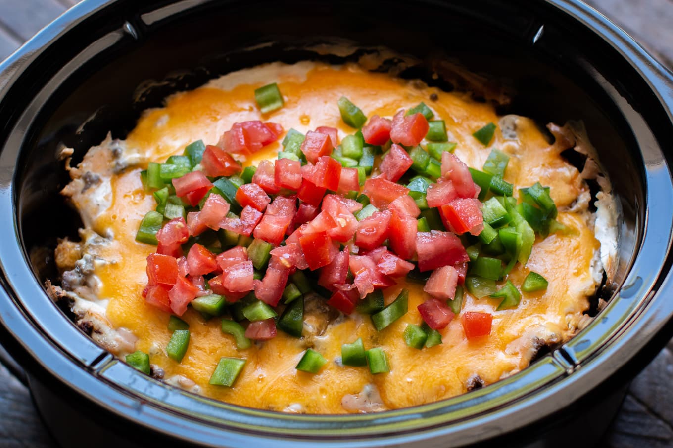 John Wayne casserole in the slow cooker with bell pepper and tomatoes on top.