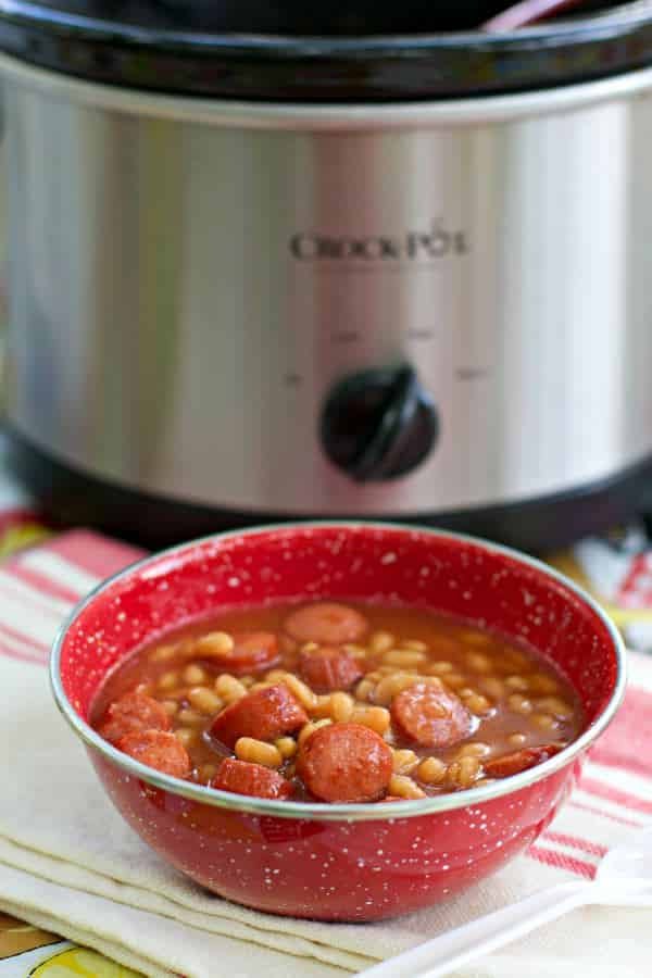 red bowl with pork and beans and hot dogs in it.