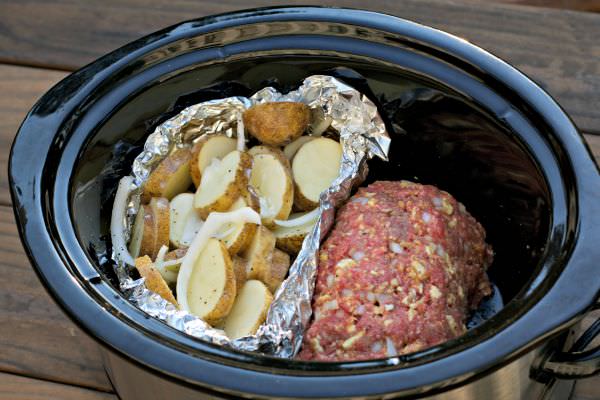 uncooked meatloaf and potatoes in foil in oval slow cooker