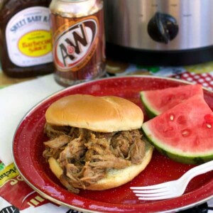 pulled pork sandwich on red plate with watermelon on the side.