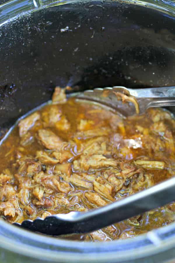 shredded root beer pulled pork in slow cooker with tongs in it.