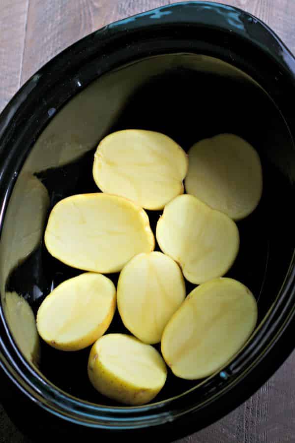 Halved yukon gold potatoes in the bottom of a slow cooker