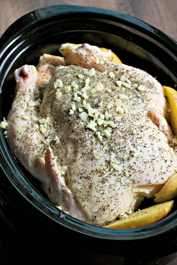 Whole chicken with garlic and seasonings, yukon gold potatoes around it, in slow cooker.
