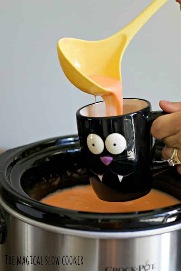 yellow ladle pouring candy corn hot chocolate into a cat mug.