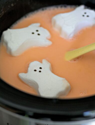 orange candy corn hot chocolate with ghost shape peeps on top.
