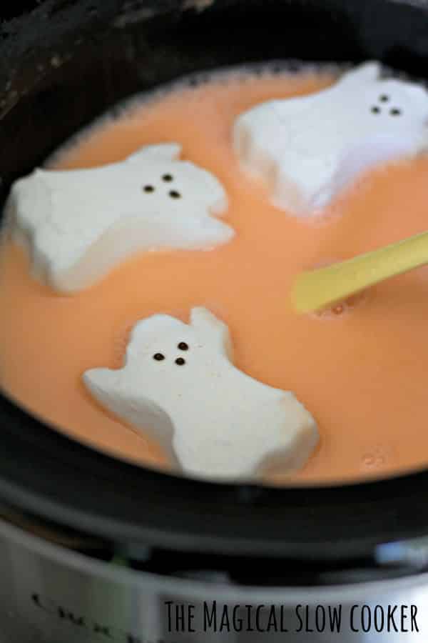 orange colored candy corn hot chocolate in the slow cooker with ghost peeps on top.