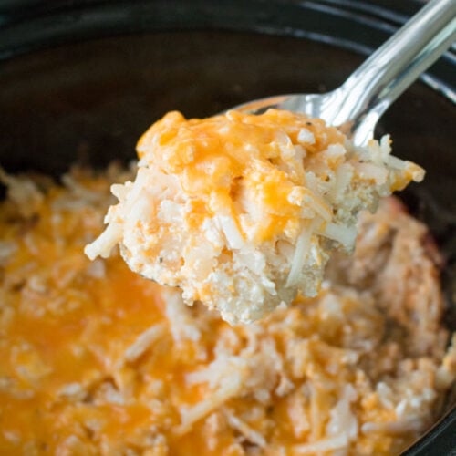 Cheesy hashbrown casserole in slow cooker with spoon scooping it out.