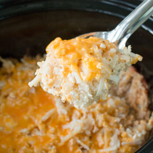 Cheesy hashbrown casserole in slow cooker with spoon scooping it out.