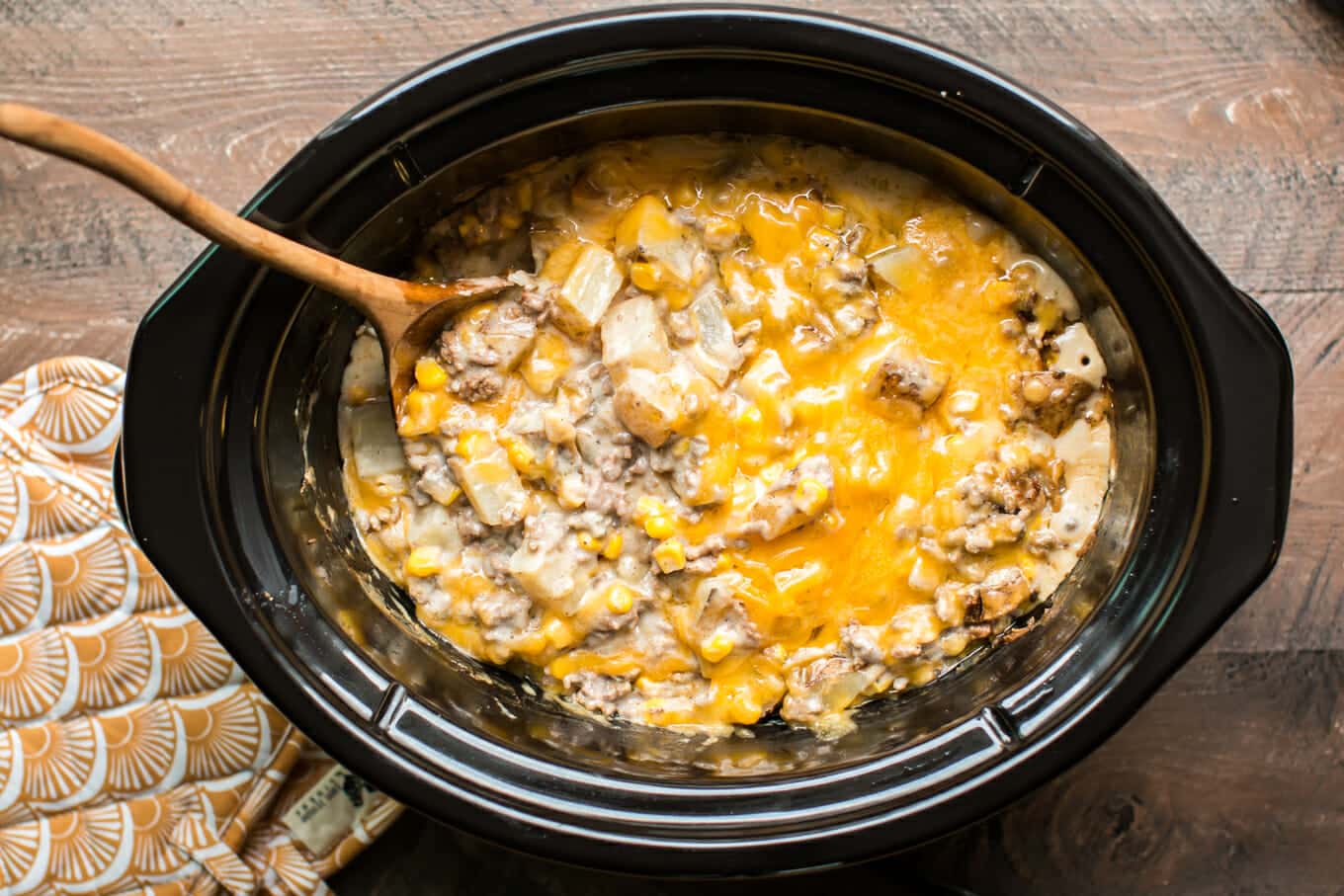 cooked hamburger hash in slow cooker with wooden spoon in it.