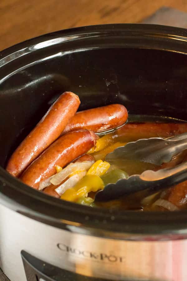 Cooked beer brats, onions and bell peppers in slow cookers.