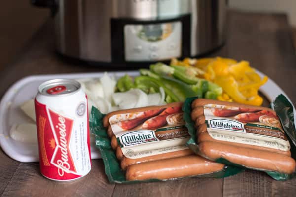 Budwiser beer, packages of brats and onion and peppers on cutting board.