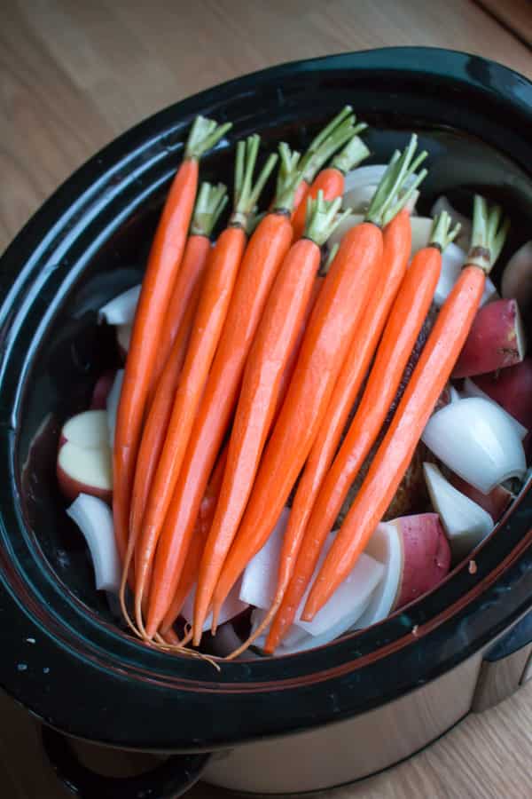 Carrots laying over beef roast in slow cooker
