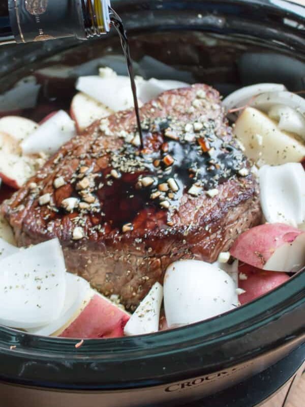 balsamic being poured over a beef roast in slow cooker