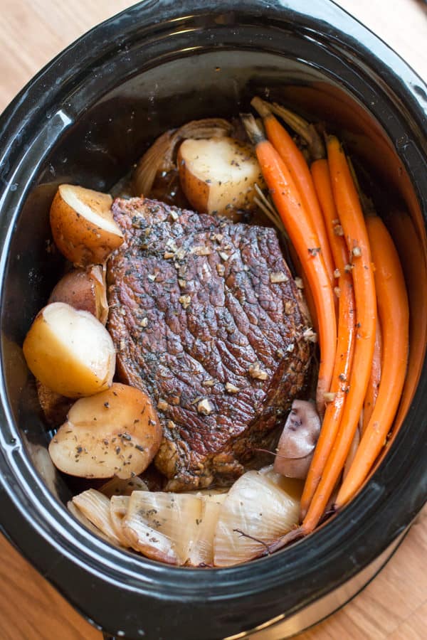Cooked beef roast in slow cooker with carrots and potatoes around it.