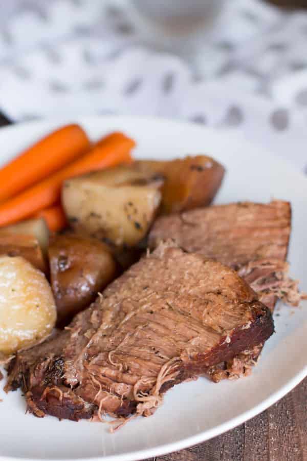 Sliced beef roast with vegetables on white plate.