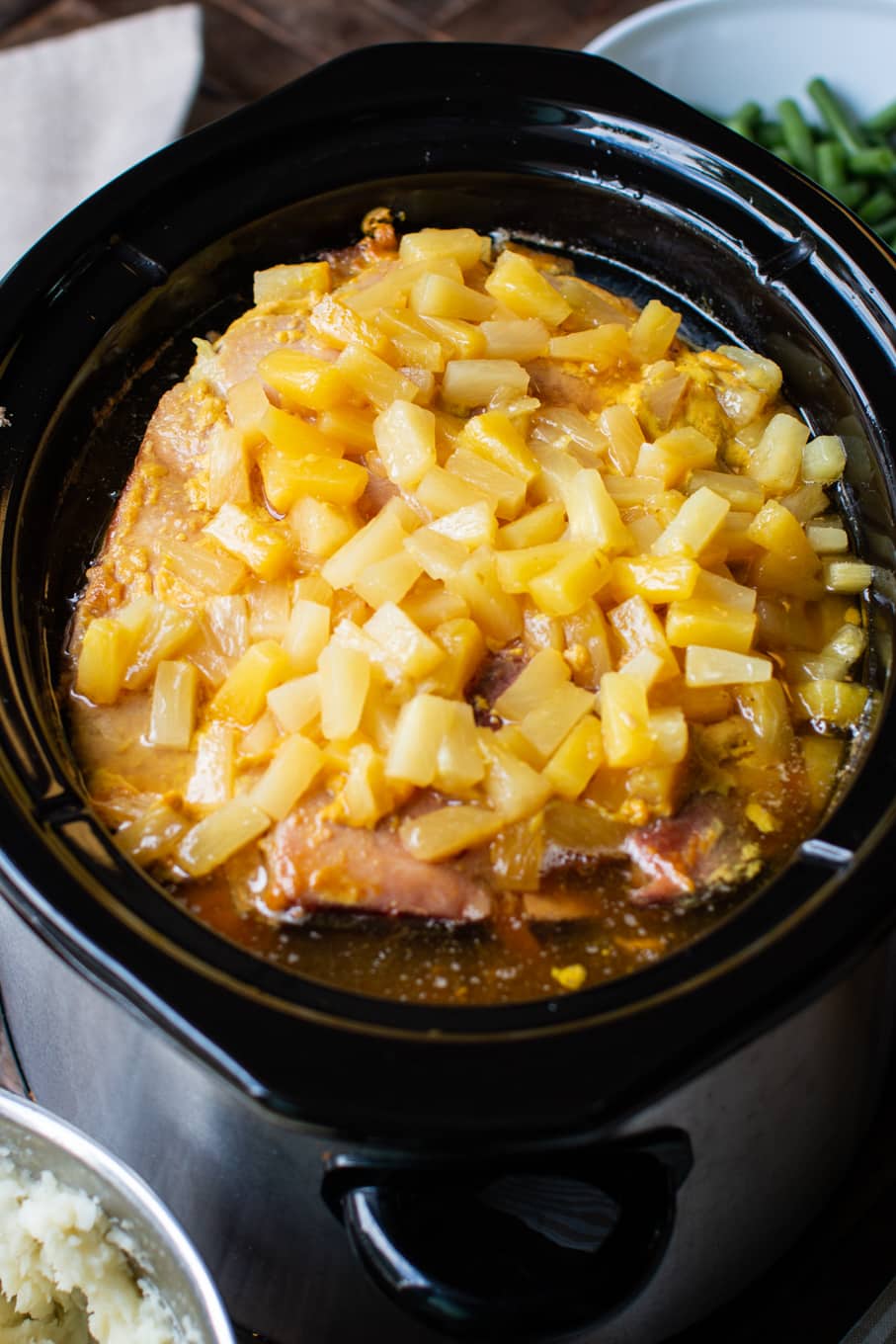 slow cooker with large ham in it, pineapples on top.