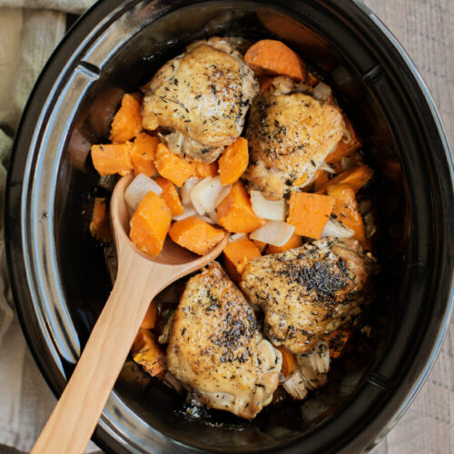 chicken, sweet potatoes and onion with wooden spoon in slow cooker.