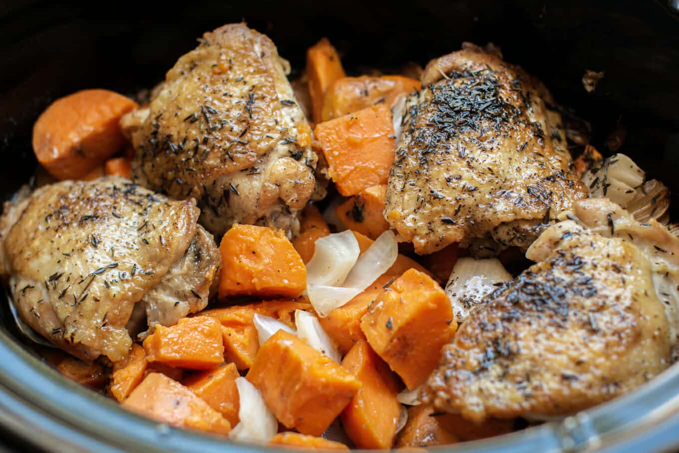 close up of chicken thighs and sweet potatoes in slow cooker.
