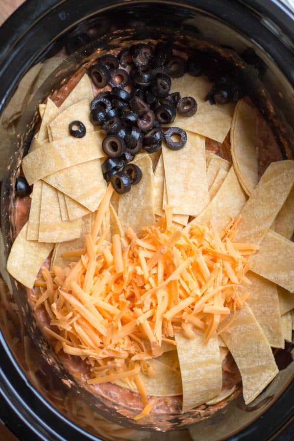 corn tortilla strips, olives, and cheese on top of shredded chicken in slow cooker.