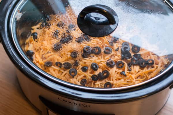 Cheese and olives on top of casserole in slow cooker with lid on.