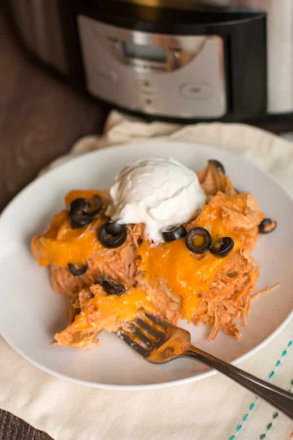 Scoop of enchilada casserole on white plate with sour cream on top.