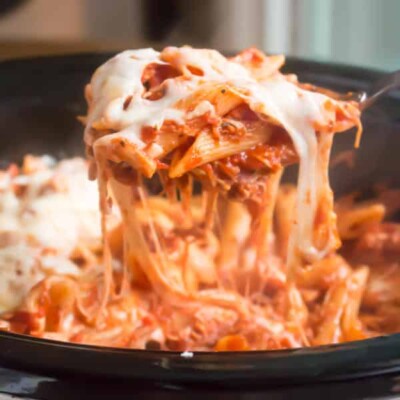 cheesy penne on spoon scooping from slow cooker