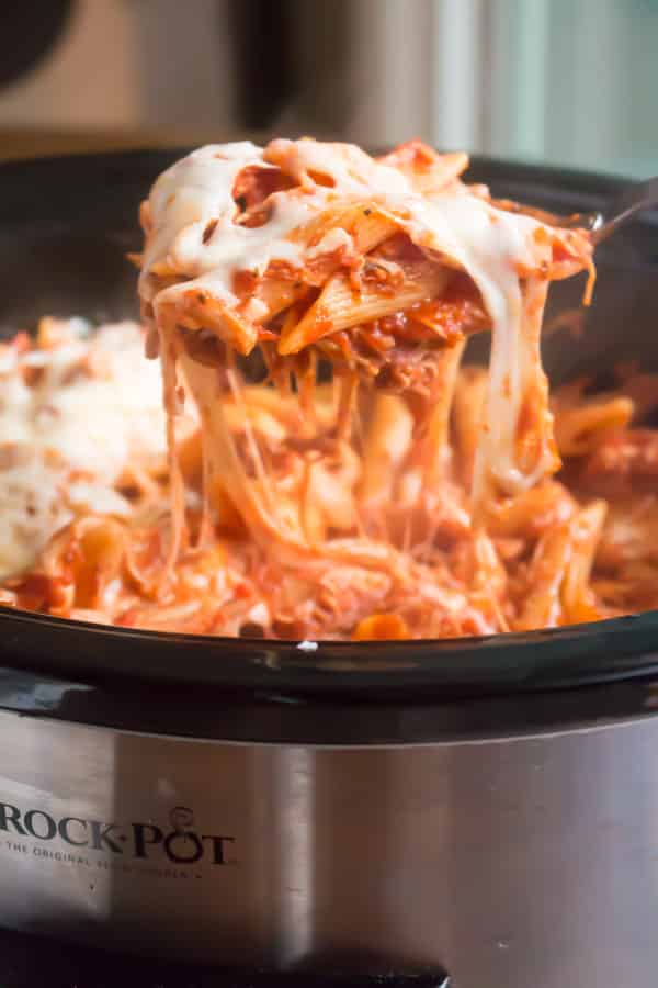 Spoon scooping out chicken Parmesan pasta from slow cooker.