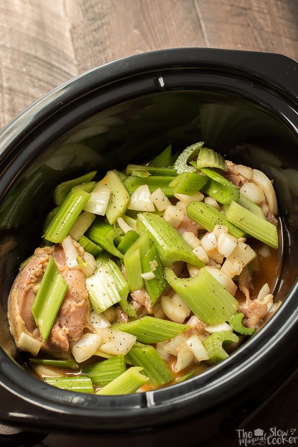 slow cooker with raw chicken, onion, and celery and black pepper.