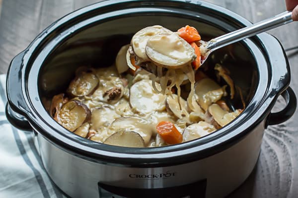 Sliced potatoes, carrots, meat, onions and sauce in slow cooker.